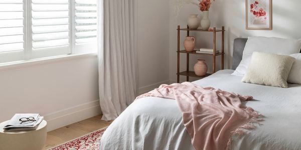 A bedroom with shutters, curtains, a textured rug and throws to keep your home warm