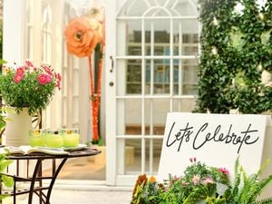 An outdoor patio with a bistro table, a planter of flowers, and a white door with a large paper flower decoration.