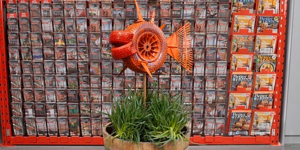 Wooden barrel with pole sticking out of it and tyre attached, painted orange. Rake sticking out of tyre.