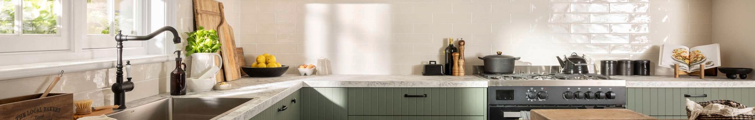 Green modern kitchen with a white marble benchtop, black sink mixer and a wooden table in it.