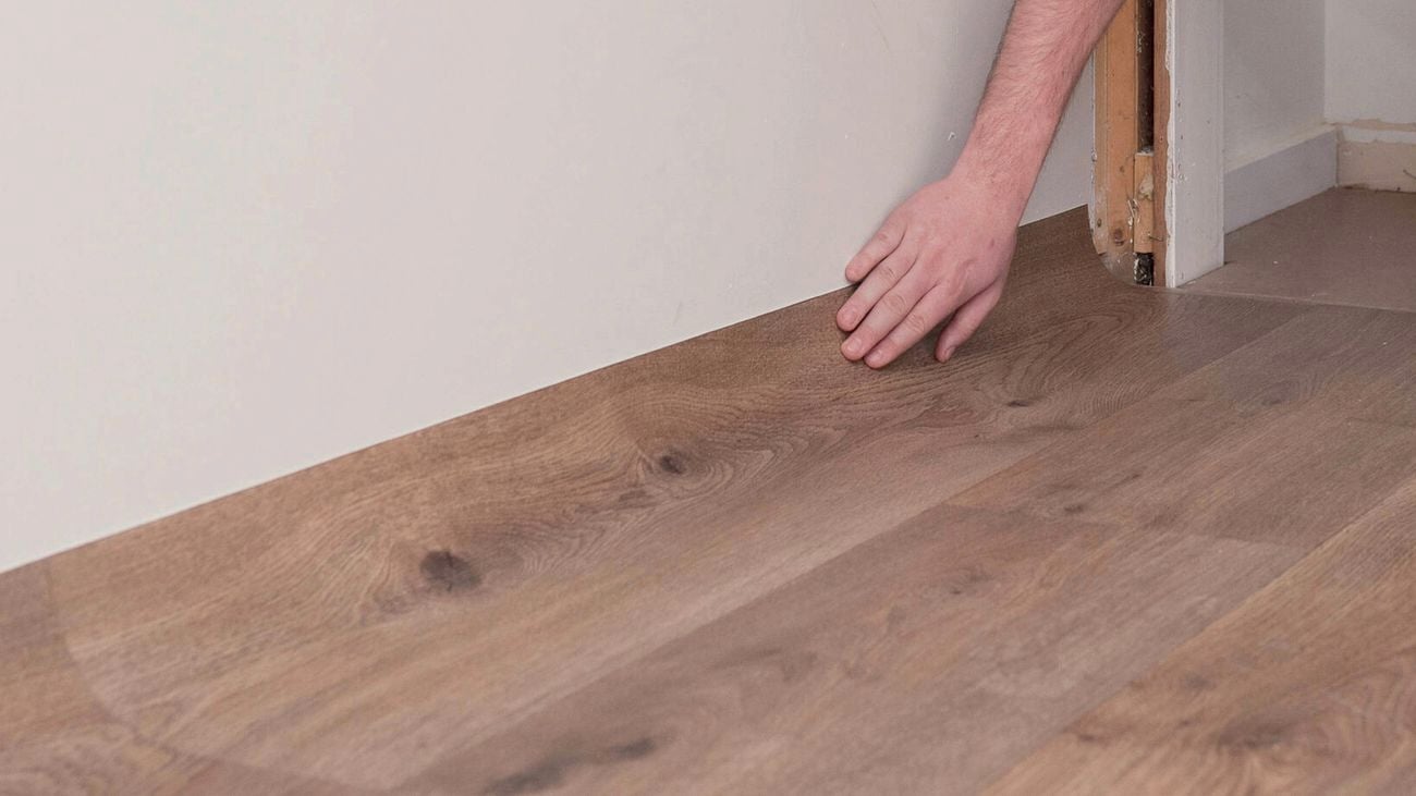 Hand installing a vinyl floorboard against a wall.