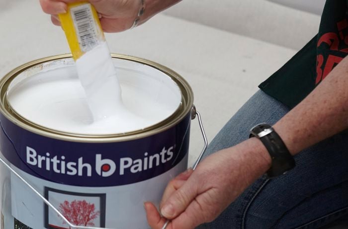 A person stirring a can of white paint