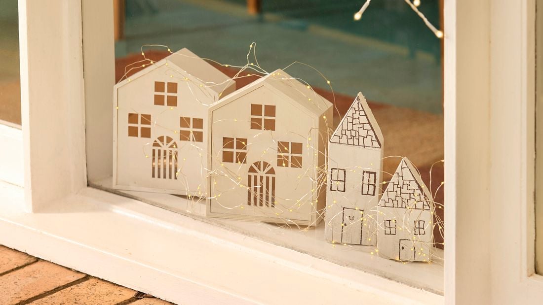 A windowsill display featuring four small white timber houses decorated with string lights.