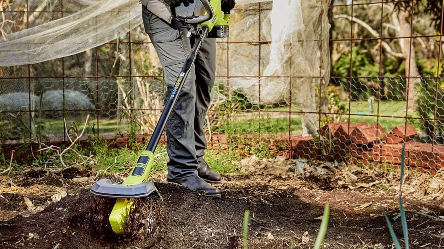 A person operating a cultivator machine in a garden.