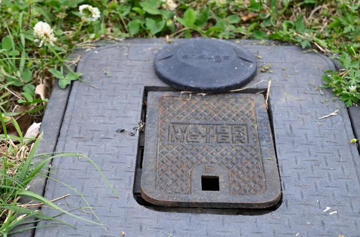 A black water meter box on the ground, in the grass.
