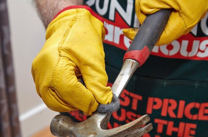 A person rubbing a rusty hammer with steel wool