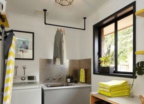 A renovated laundry with towels, a ironing board, hanging clothes and a washing machine.