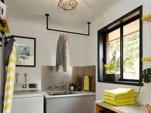A renovated laundry with towels, a ironing board, hanging clothes and a washing machine.