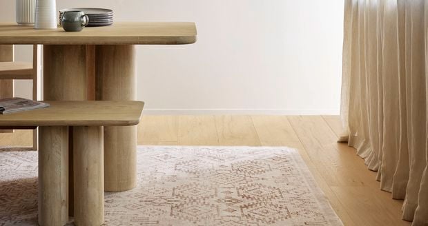Dining table with crockery on it sitting on a rug on floorboards.