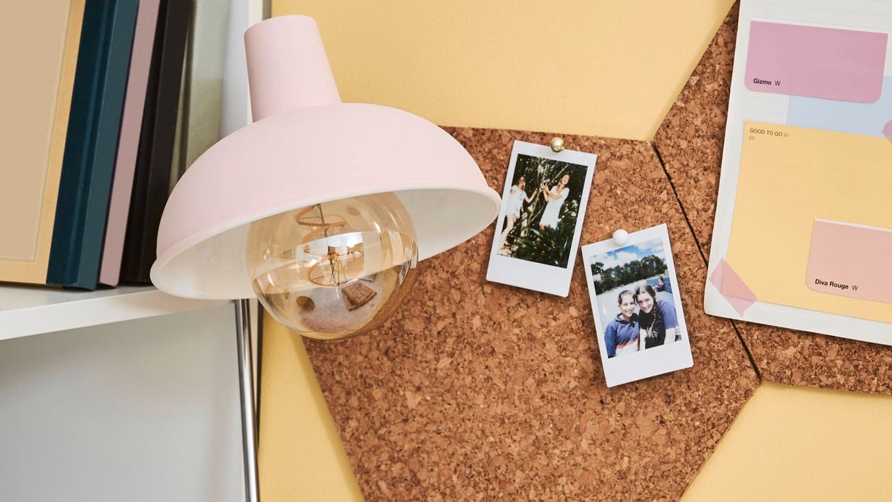 A teenagers desk space decorated with a pink lamp, notebooks and hexagon cork tiles