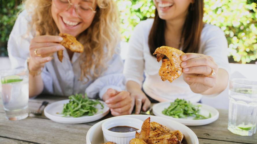 Two people enjoying seasoned chicken wings and salad together at an outdoor dining table.