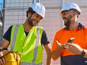 Two tradesman on a jobsite wearing PPE with a phone.