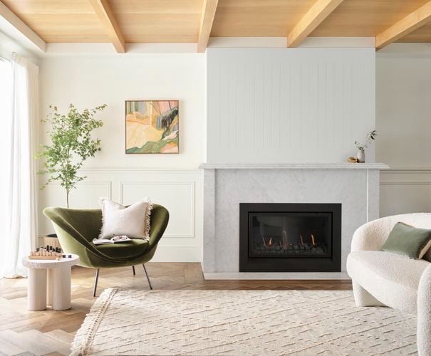 Bright living room with marble fireplace and gas fire, armchairs, a rug and a tall plant in the corner