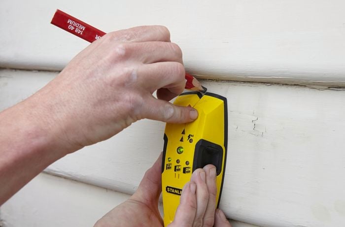 A stud finder being used to locate the stud wall behind weatherboards