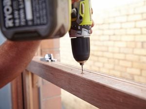 Person using a cordless drill to drill a hole in a sash window frame