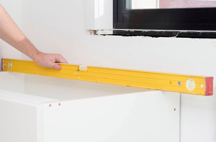 A person is using a spirit level to check if the top of a corner base cabinet is even.