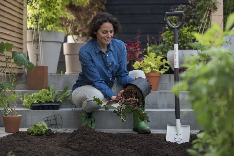 A woman upending a pot plant to transfer into a garden bed