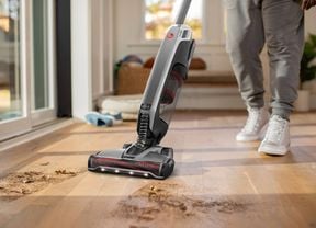 Person using a stick vacuum inside a house