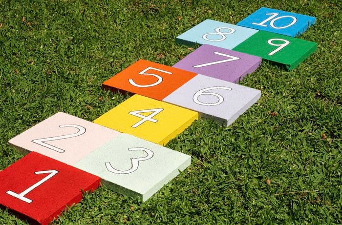 Bright painted paver tiles with numbers are arranged on grass to form a reusable hopscotch path for kids to play outdoors.