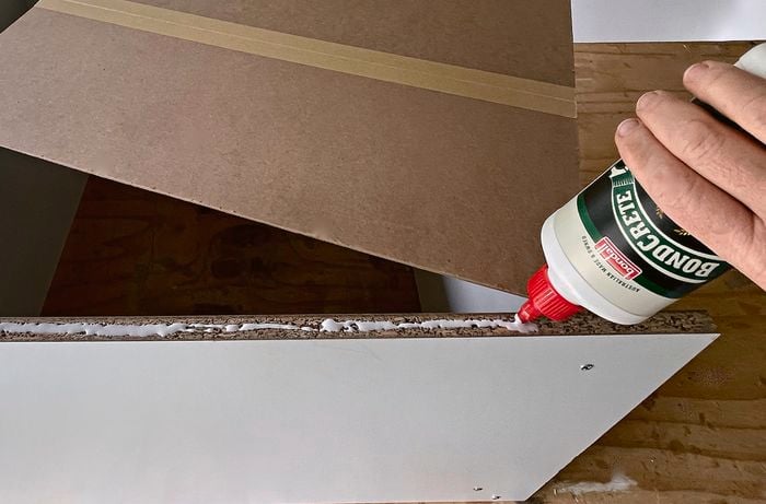 A person glues a backing piece to a cupboard] 