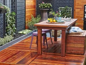 Outdoor decking with wooden table, stools and plants around the fence.