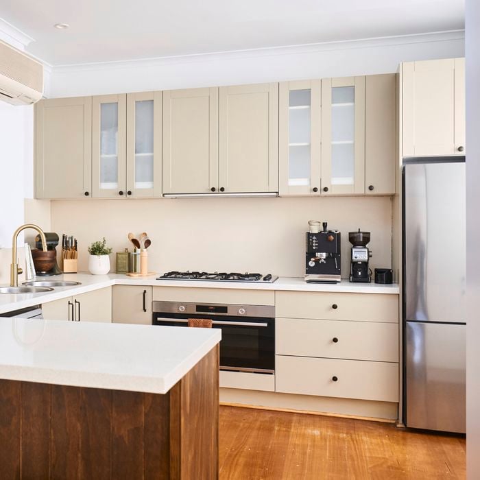 Bright modern kitchen with cream cabinetry, white benchtops, stainless steel appliances, timber island bench and a wall-mounted split-system air conditioner.