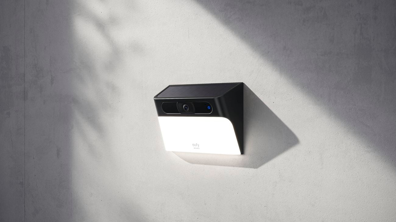 White security camera mounted high up on a white wall, outdoors.