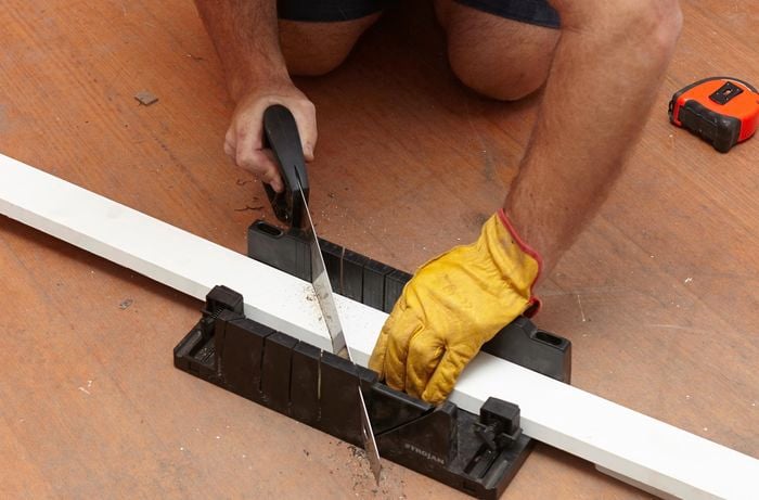 A person cutting architrave with a hand saw and mitre box