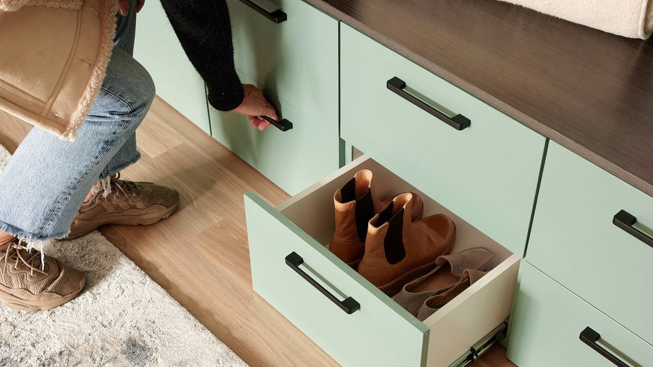 Shoe drawer open with shoes inside and person holding drawer handle.