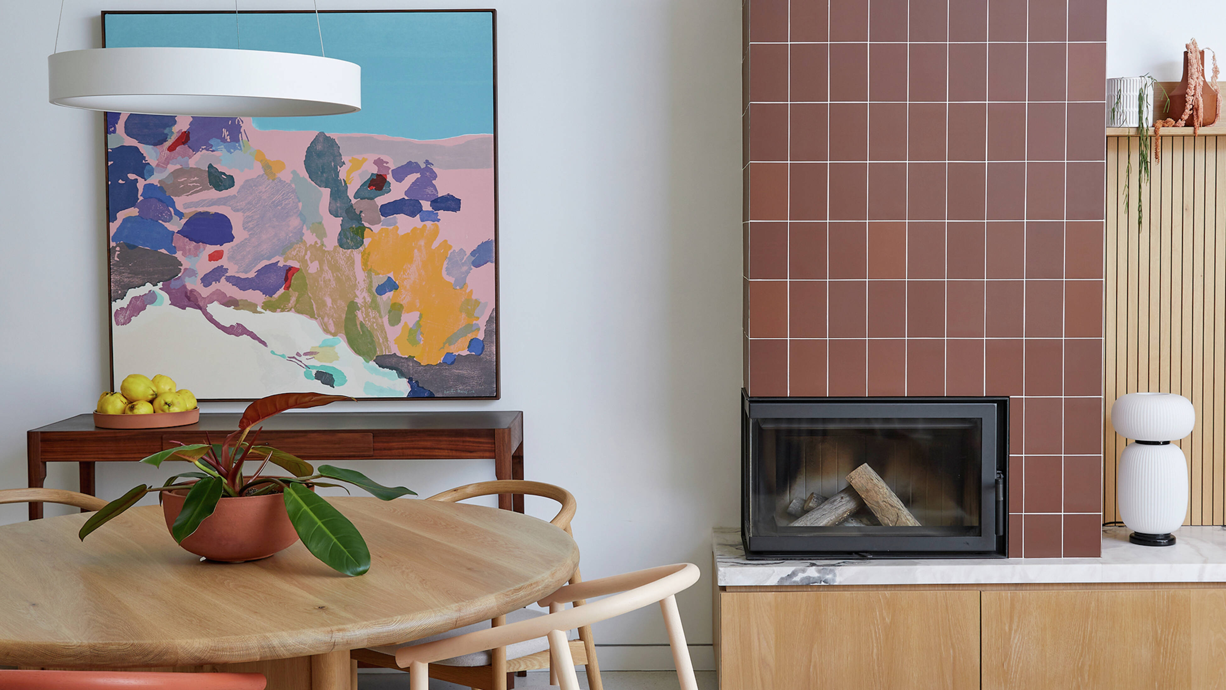 A modern dining and living space featuring a current tiling trend – a tiled fireplace as a visual point of interest, a marble benchtop and warm wood tones.