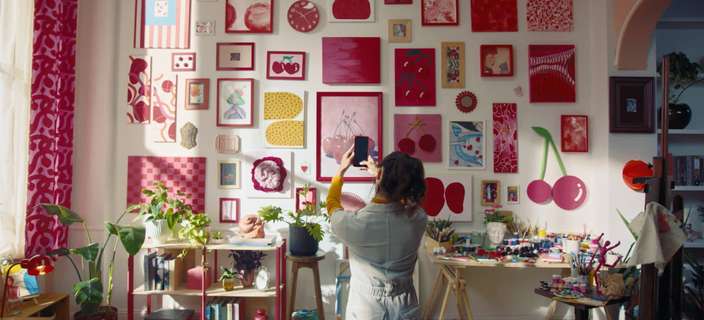 Person photographing a colourful gallery wall of cherry-themed artwork displayed using 3M Command Picture Hanging products.