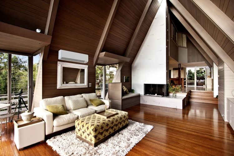 Interior of triangle-shaped timber building with white couch, white mirror and air conditioning unit