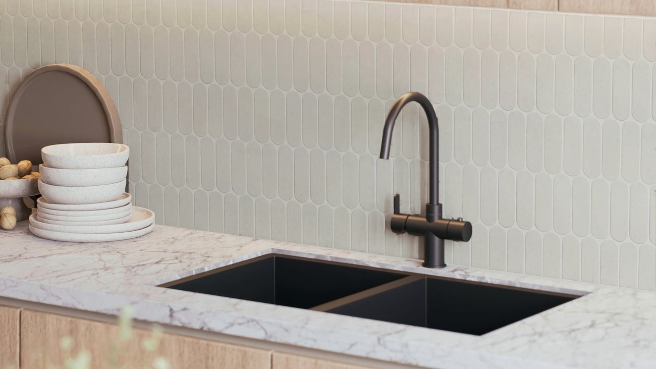 Kitchen sink with a matte black mixer tap set into a white stone benchtop, featuring light hexagon tile splashback and timber cabinetry.