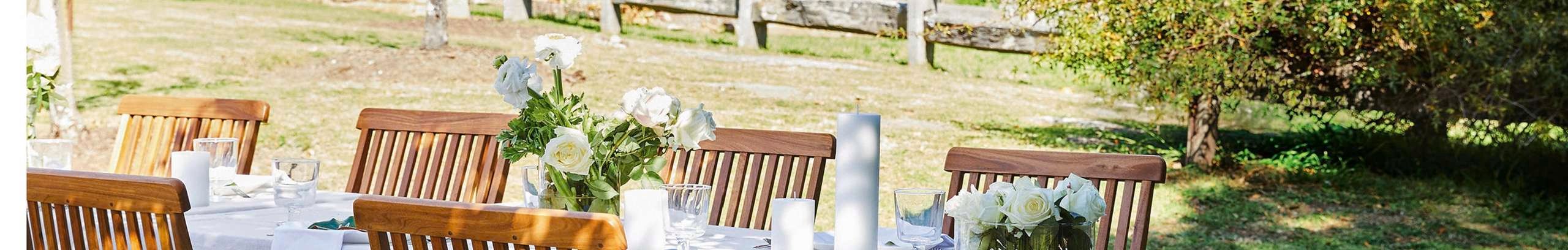 An outdoor wedding table setting in a secluded backyard. Hessian tablecloth and white flowers adorn the timber table setting.