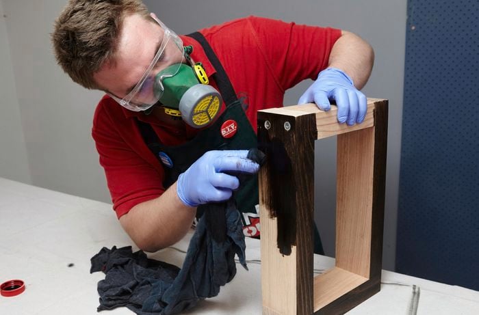 A person applying black stain to a timber rectangle