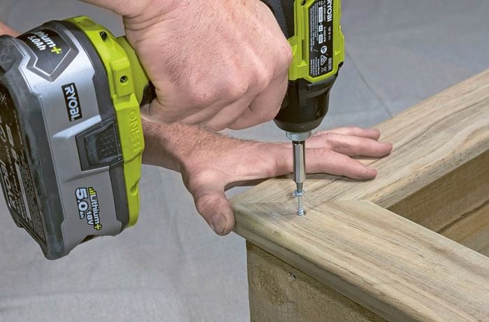 A person screwing a mitred capping onto a wooden planter box.