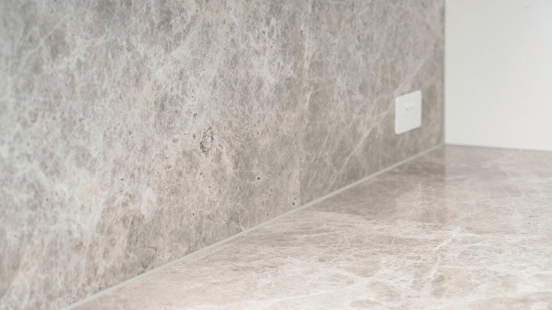 Finished stone-look benchtop and splashback with a clean, continuous silicone seal visible along the joint after application and cleanup.