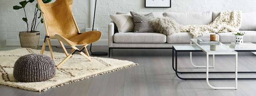 Room with wooden flooring along with a couch, black and white tables, rug, chair, plant and light. 