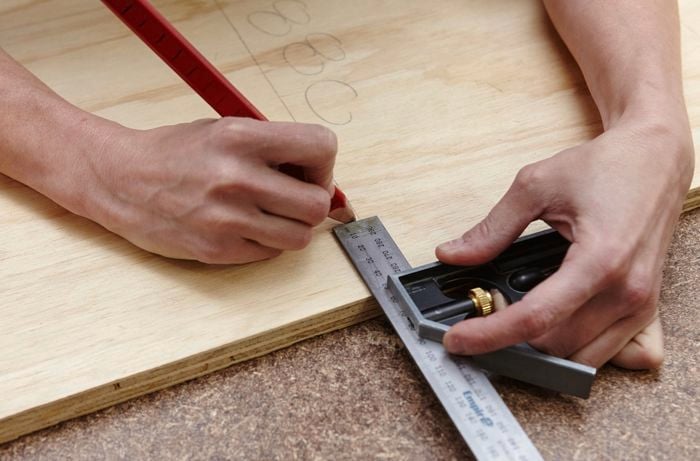 A person using a combination square to mark a measurement on a sheet of plywood