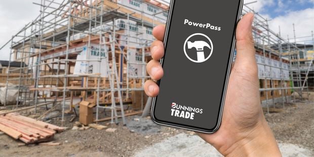 A hand holding a phone with the PowerPass app open on a construction site