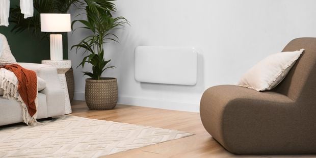 Heater on a wall in a lounge room with a chair with a cushion on it and a pot plant