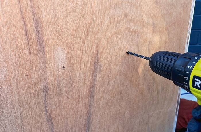A drill bit creating a hole in a piece of plywood