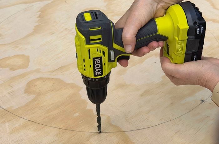  A close up image of a Ryobi drill, drilling into plywood that has a pencil circle drawn on it.