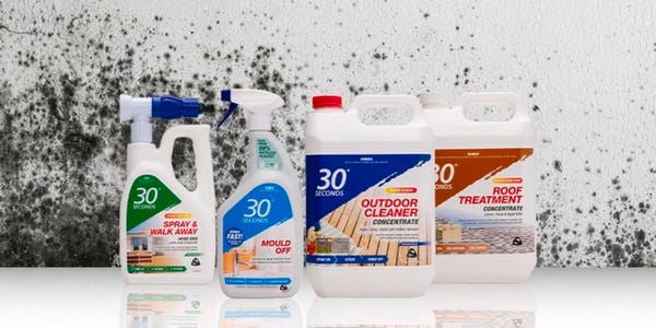 Four bottles of 30 second cleaner in front of a white wall that has mould on it.