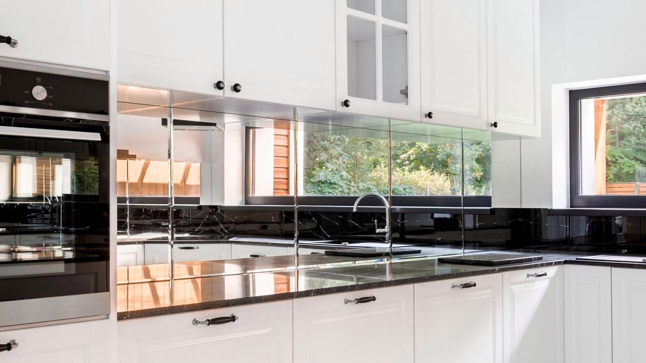 White kitchen with black stone benchtops, white cabinetry, a black sink and tap, and a reflective mirror splashback beneath overhead cupboards.
