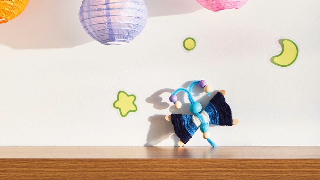 A D.I.Y. Bluey craft Flappy project sits on a timber shelf with a star, moon, planet and two Bluey lanterns about it.