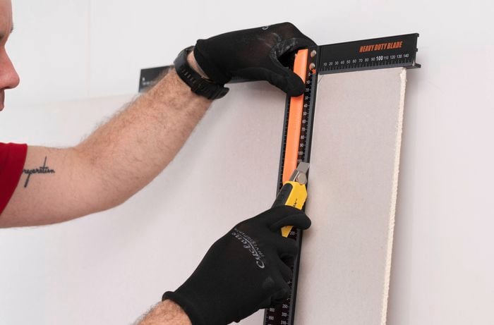 A person in black gloves cutting plasterboard with a utility knife and a Professional Drywall T-Square