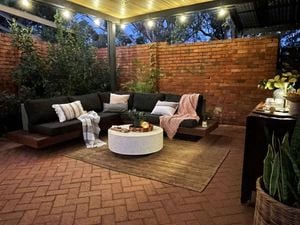 Outdoor timber floating lounge with grey cushions, throw rug, coffee table sitting in front with red brick wall in back ground