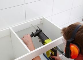 Person using a power drill to fix a bathroom vanity to a tiled wall