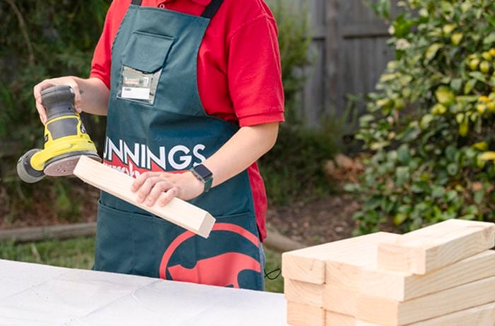 Bunnings team member sanding the end of a piece of timber with an orbital sander